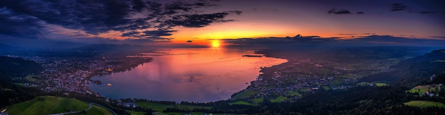 A sunset over a lake with a town in the foreground and mountains in the background.