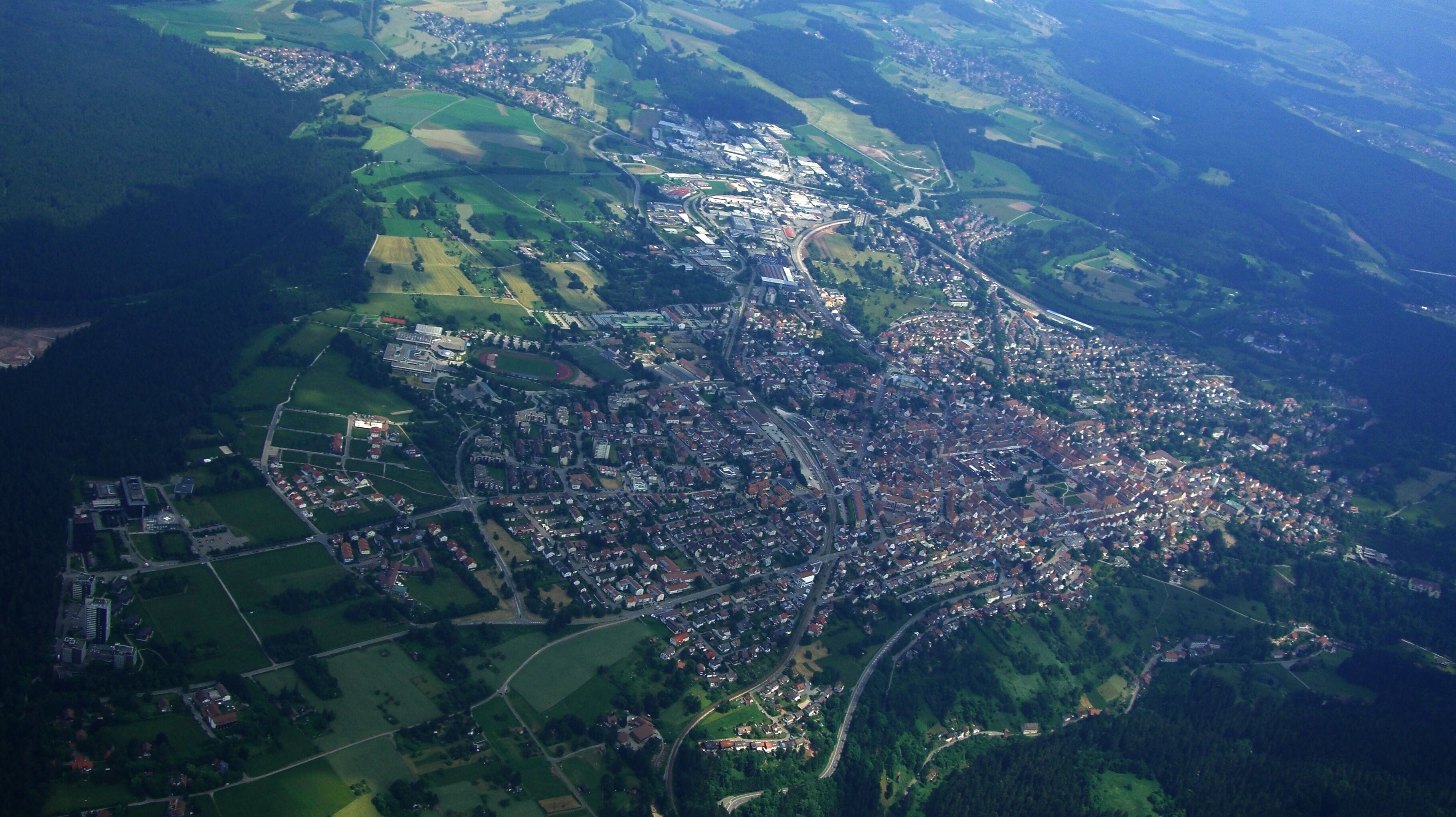 An aerial view of a town with a dense cluster of buildings, surrounded by green fields and a river.