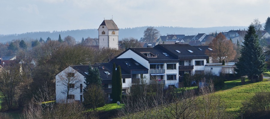 Ein Wohngebiet mit einem markanten Kirchturm, Häusern und einer hügeligen Landschaft im Hintergrund.