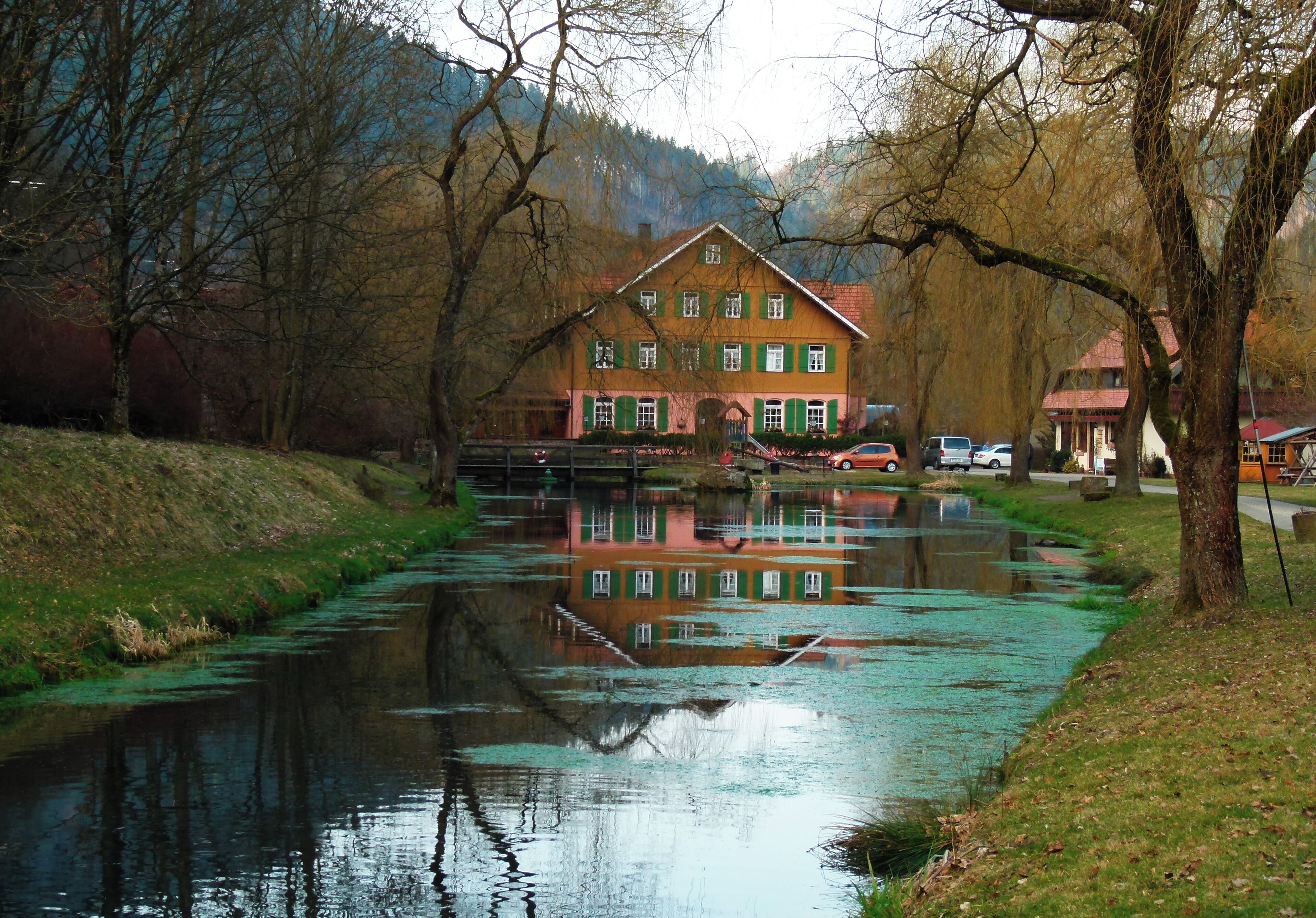 A house with green shutters and a reflection in a calm river.