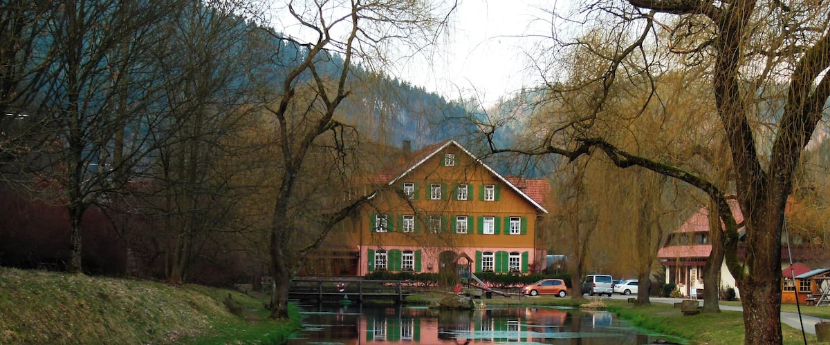 A house with green shutters and a reflection in a calm river.