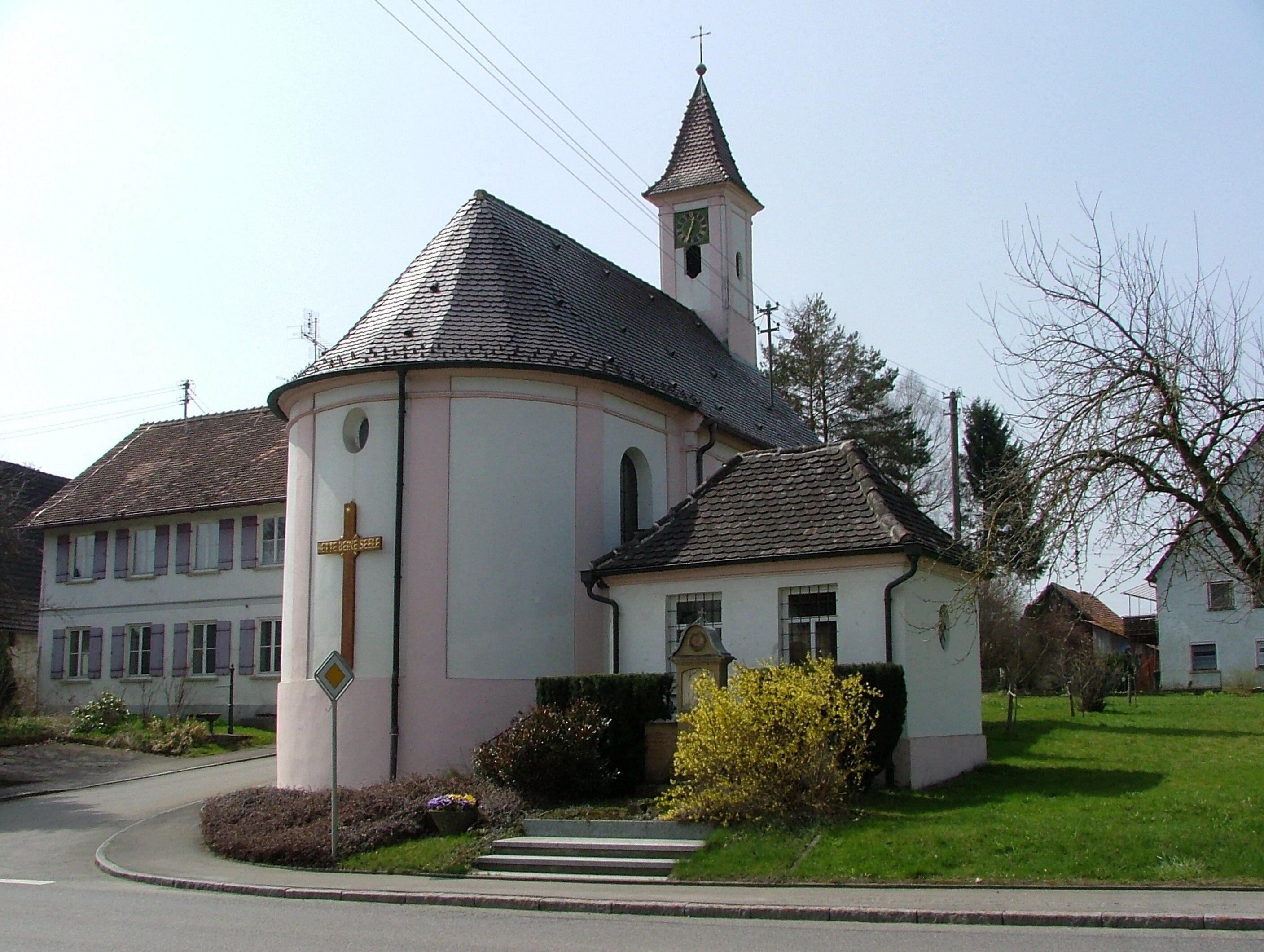 A church with a bell tower and a clock, surrounded by a well-maintained lawn and a road.