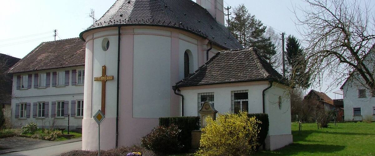 A church with a bell tower and a clock, surrounded by a well-maintained lawn and a road.