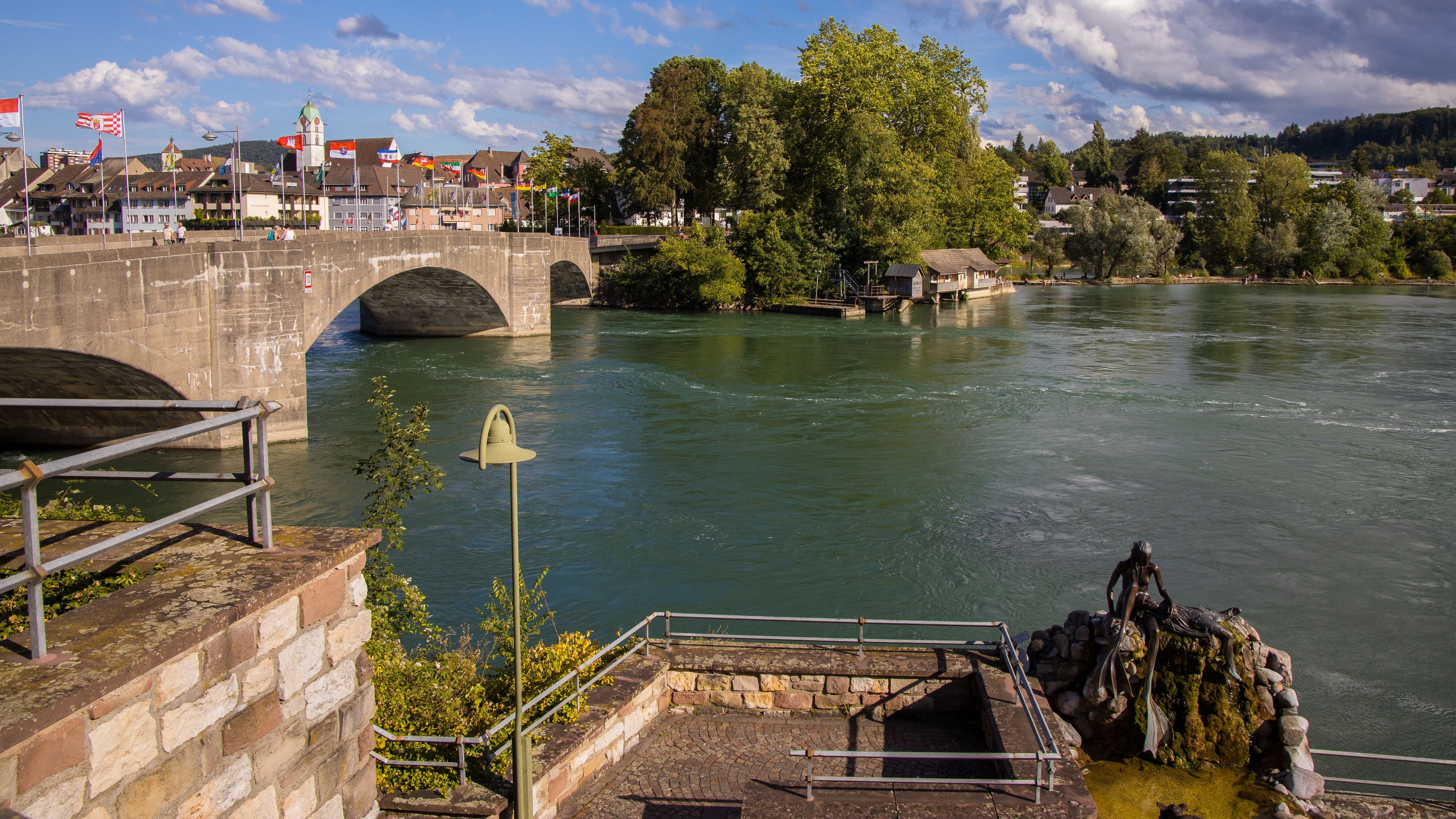 A river with a stone bridge, a bell, and a town in the background.