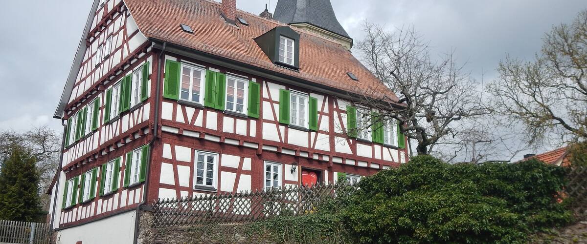 A traditional half-timbered house with a steeply pitched roof and a church steeple.