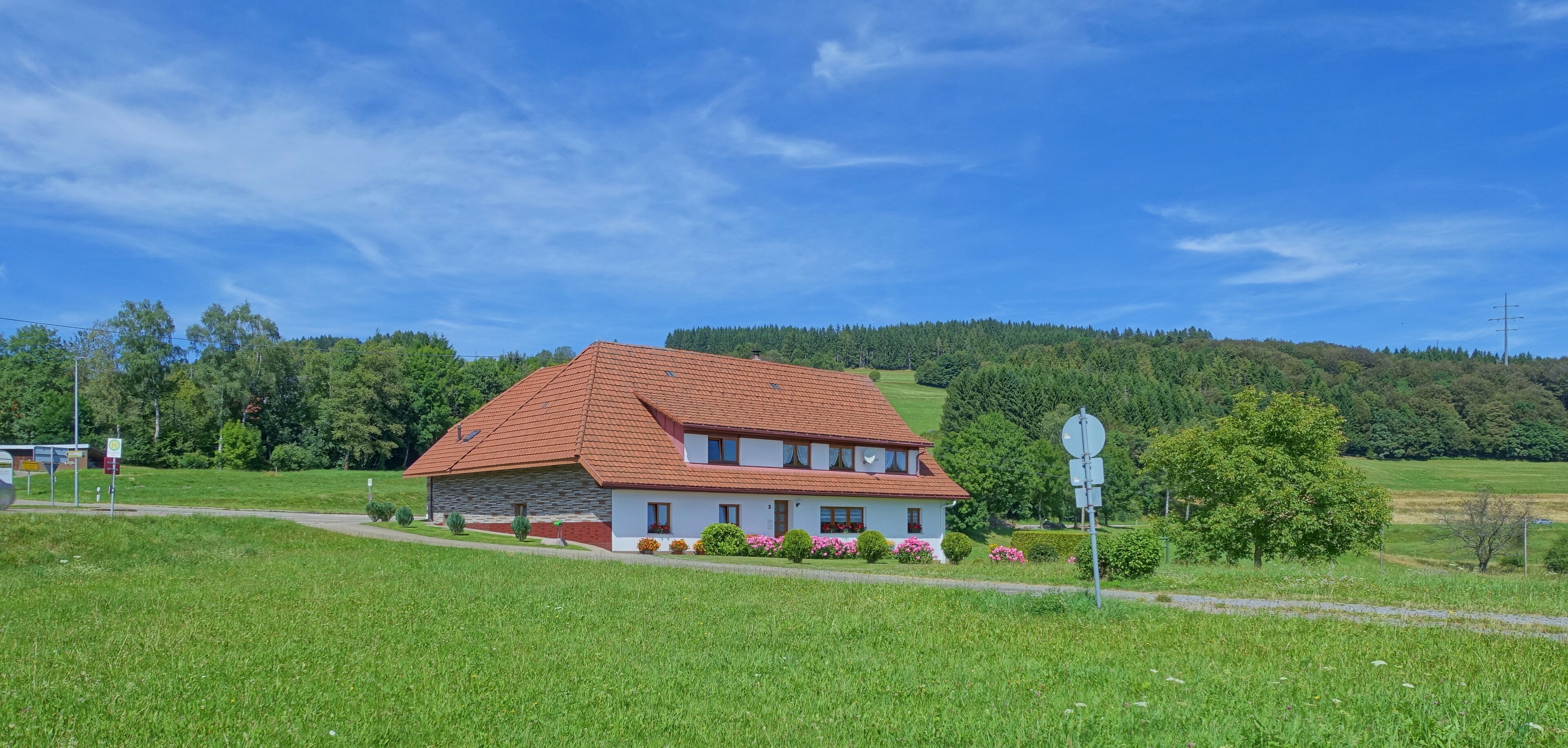A house with a red roof and white walls, surrounded by green fields and trees.