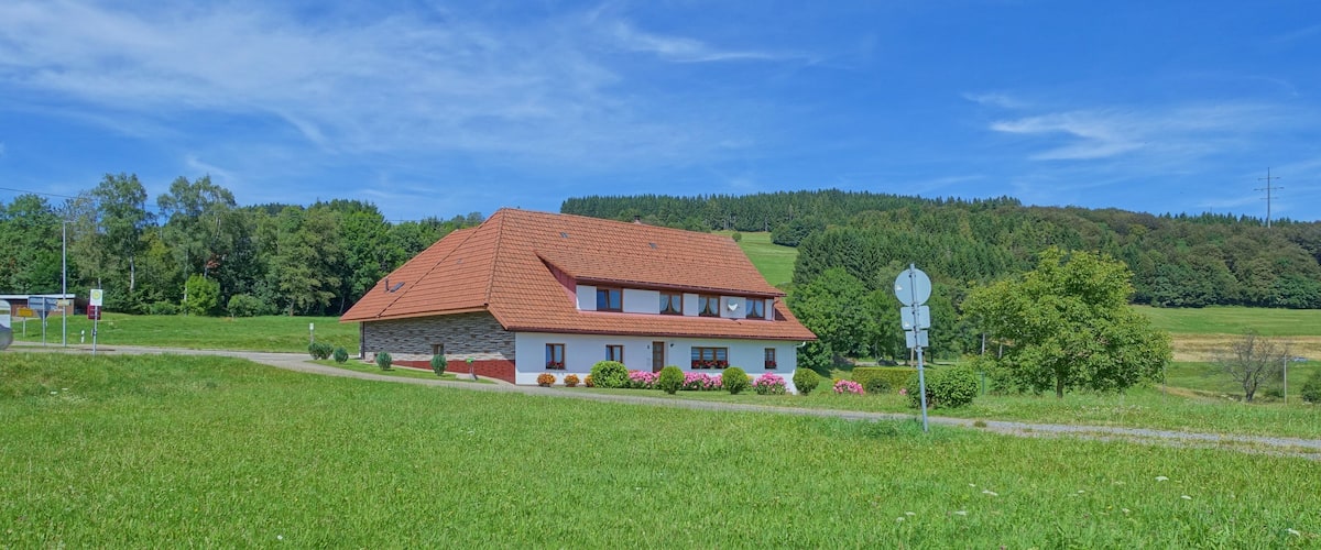 A house with a red roof and white walls, surrounded by green fields and trees.