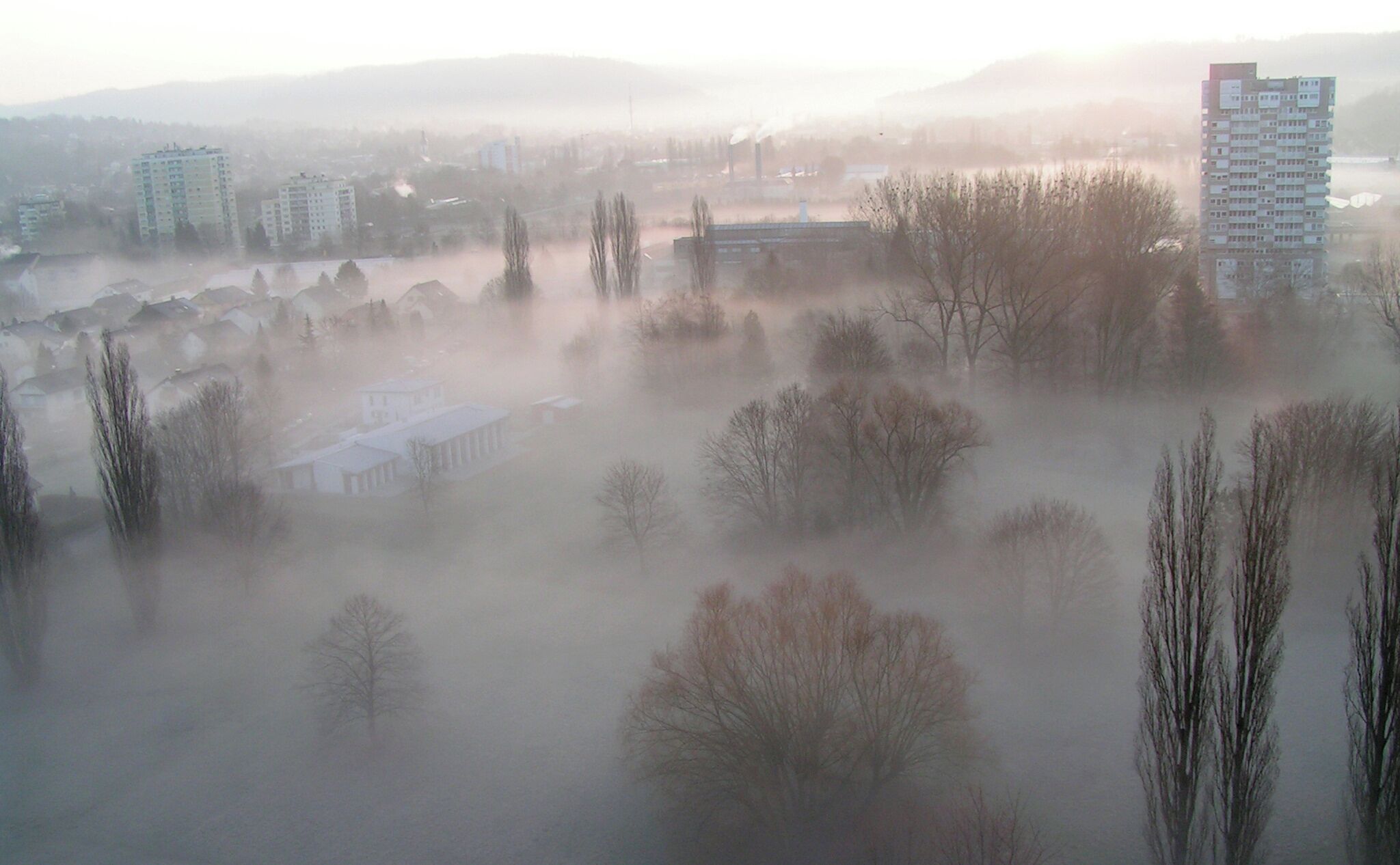 A foggy landscape with buildings, trees, and a river.