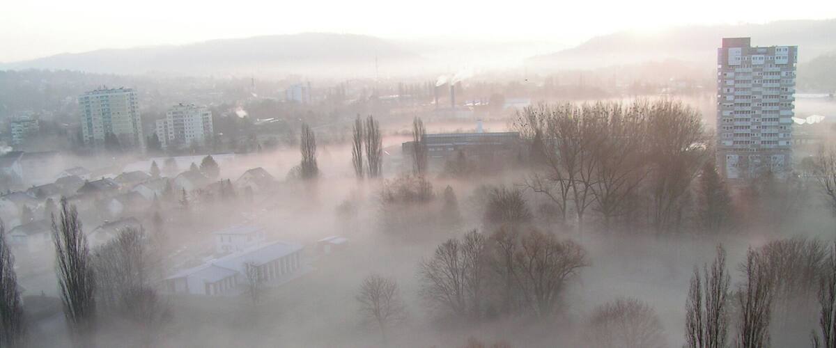 A foggy landscape with buildings, trees, and a river.