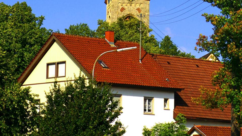 A church with a clock tower, surrounded by trees and a house with a red roof.