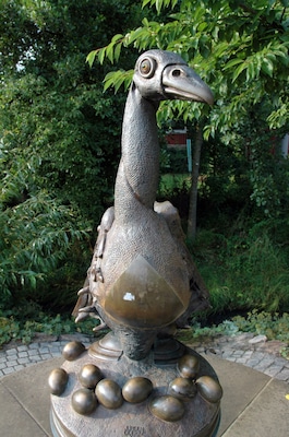 Una escultura de bronze d'un ocell amb coll llarg i grans ulls, envoltat per esferes de bronze més petites.