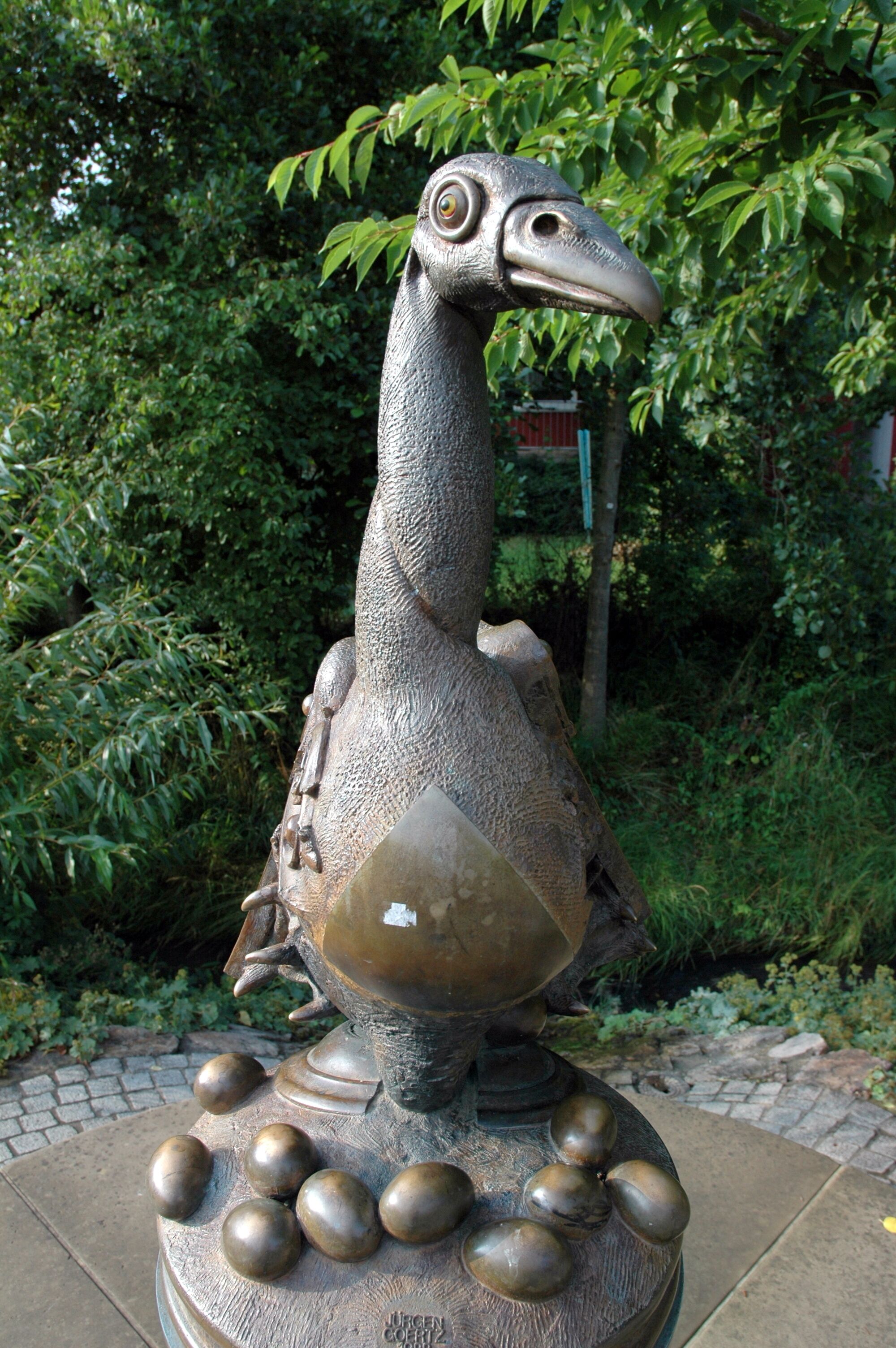 A bronze sculpture of a bird with a long neck and large eyes, surrounded by smaller bronze spheres.