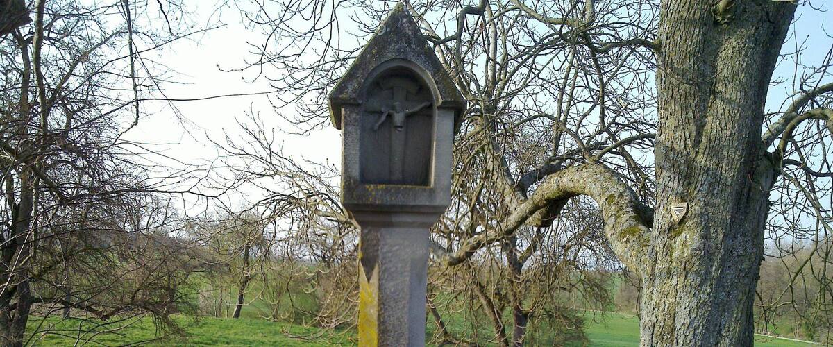 A stone cross with a crucifix, surrounded by grass and trees.