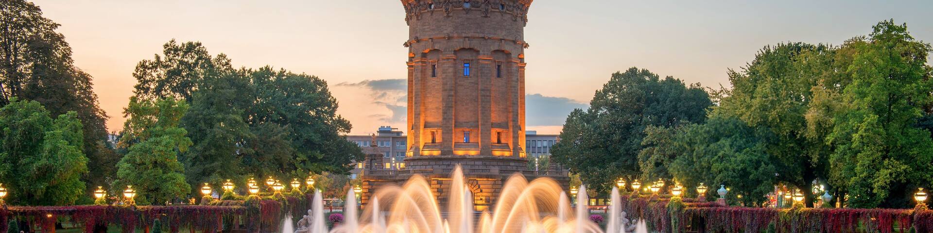 A historic tower with a spire, surrounded by a well-manicured garden with a central fountain.