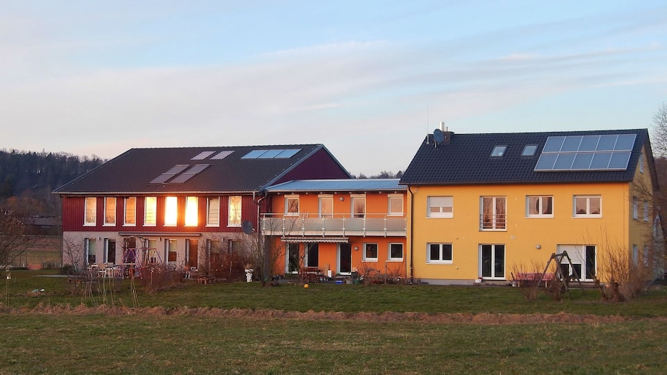 A row of houses with solar panels, a playground, and a forested hill in the background.