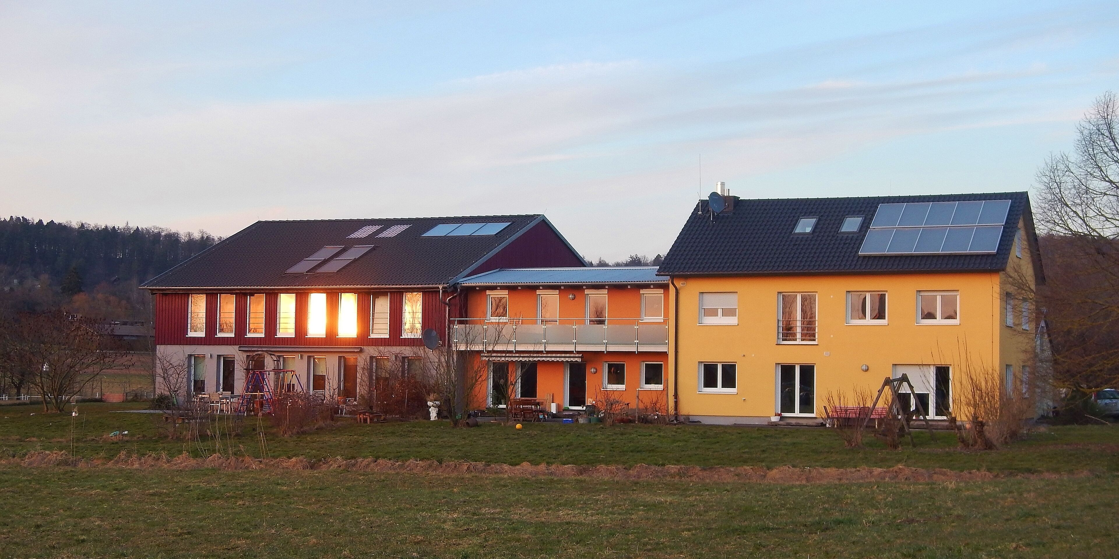 A row of houses with solar panels, a playground, and a forested hill in the background.
