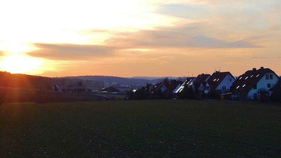 A sunset over a residential area with houses and a field.