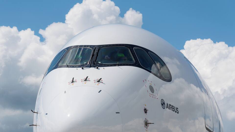 A large white airplane with the AIRBUS logo, set against a blue sky with clouds.