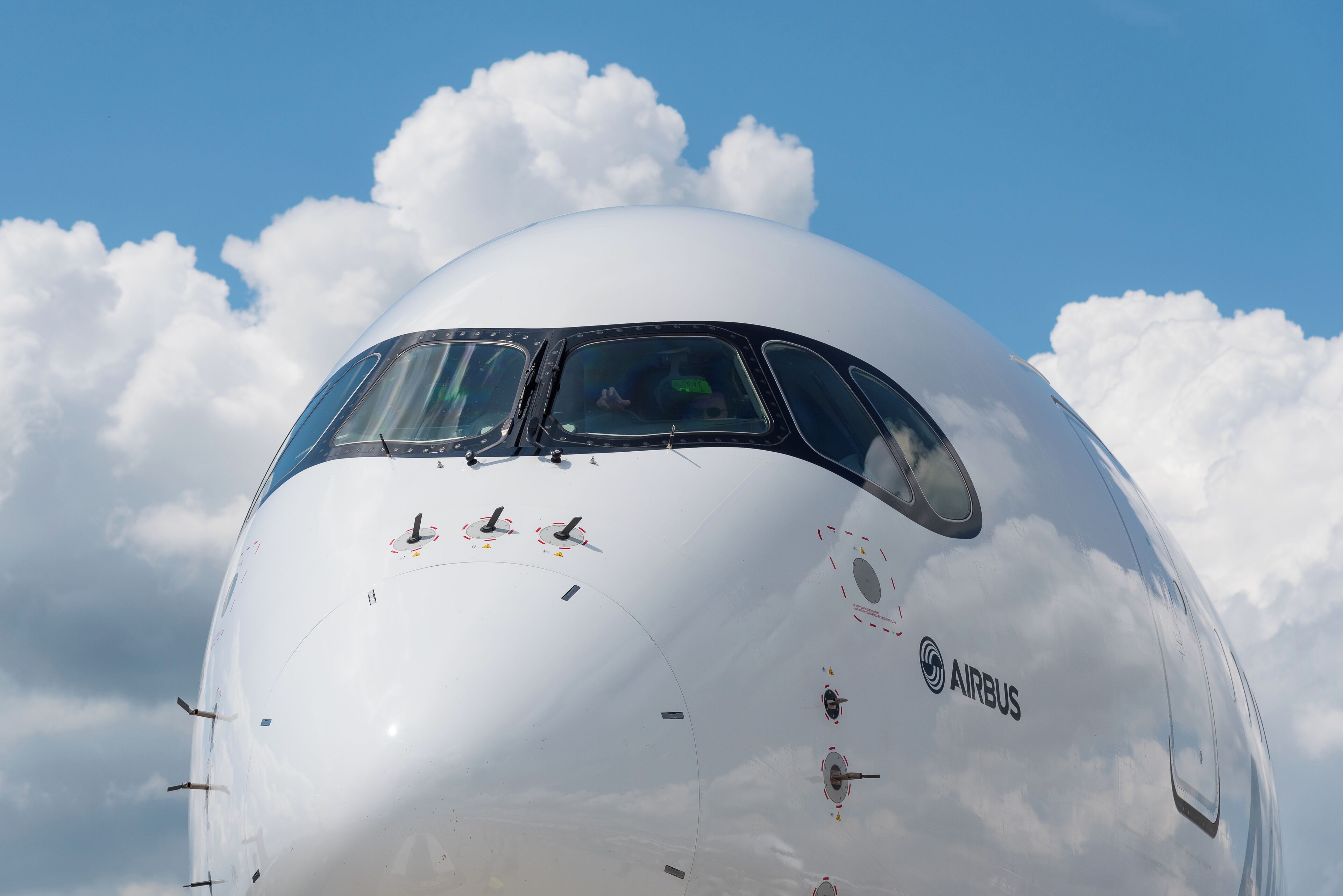 A large white airplane with the AIRBUS logo, set against a blue sky with clouds.