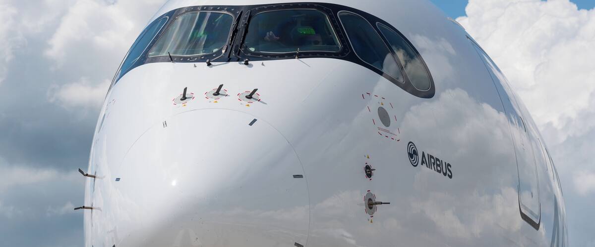 A large white airplane with the AIRBUS logo, set against a blue sky with clouds.