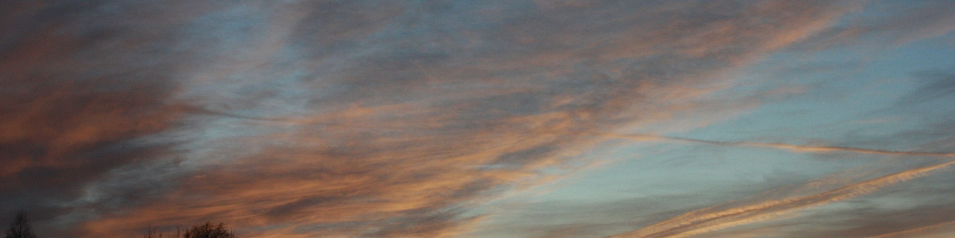 Un atardecer con un cielo lleno de nubes y la silueta de árboles.