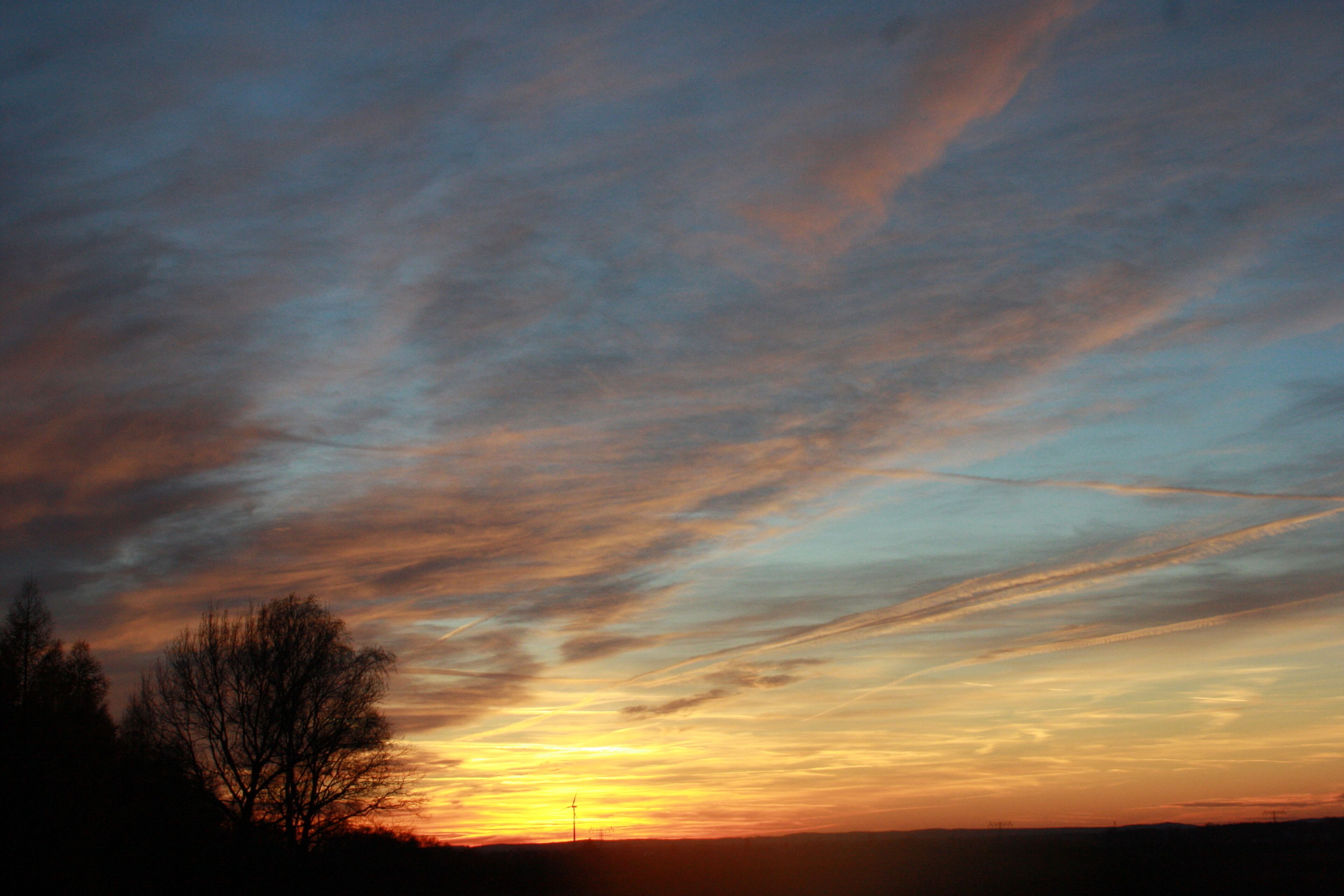 A sunset with a sky filled with clouds and a silhouette of trees.