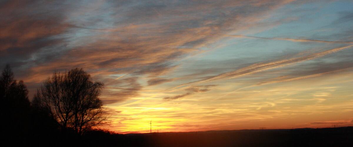A sunset with a sky filled with clouds and a silhouette of trees.