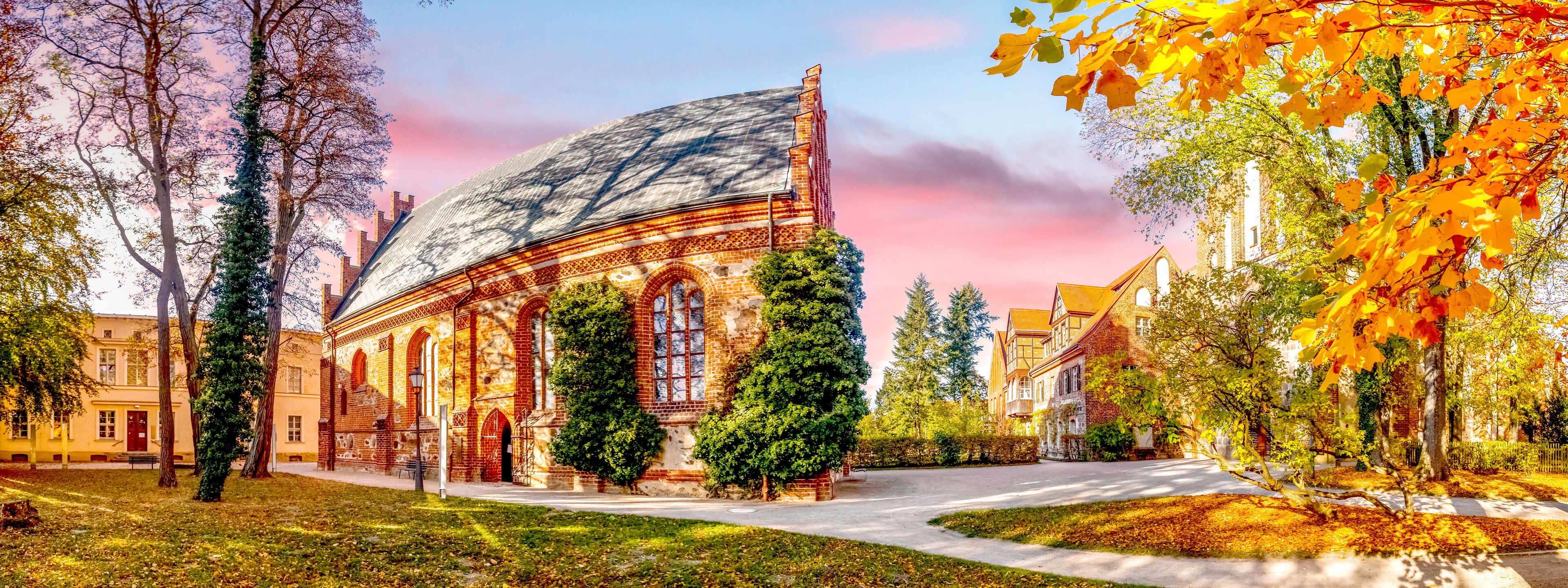 A historic building with a large arched roof, surrounded by trees and a well-maintained lawn.