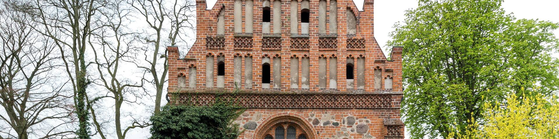 A historic brick building with a tall, pointed roof and a large arched window.