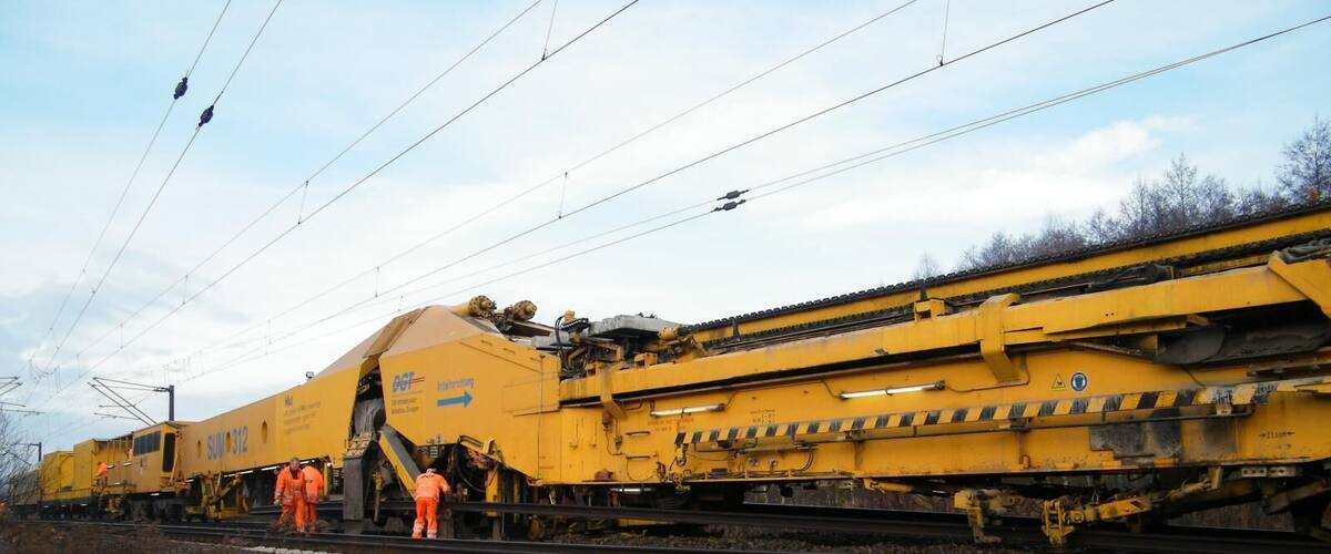 A large yellow train with workers on the tracks.