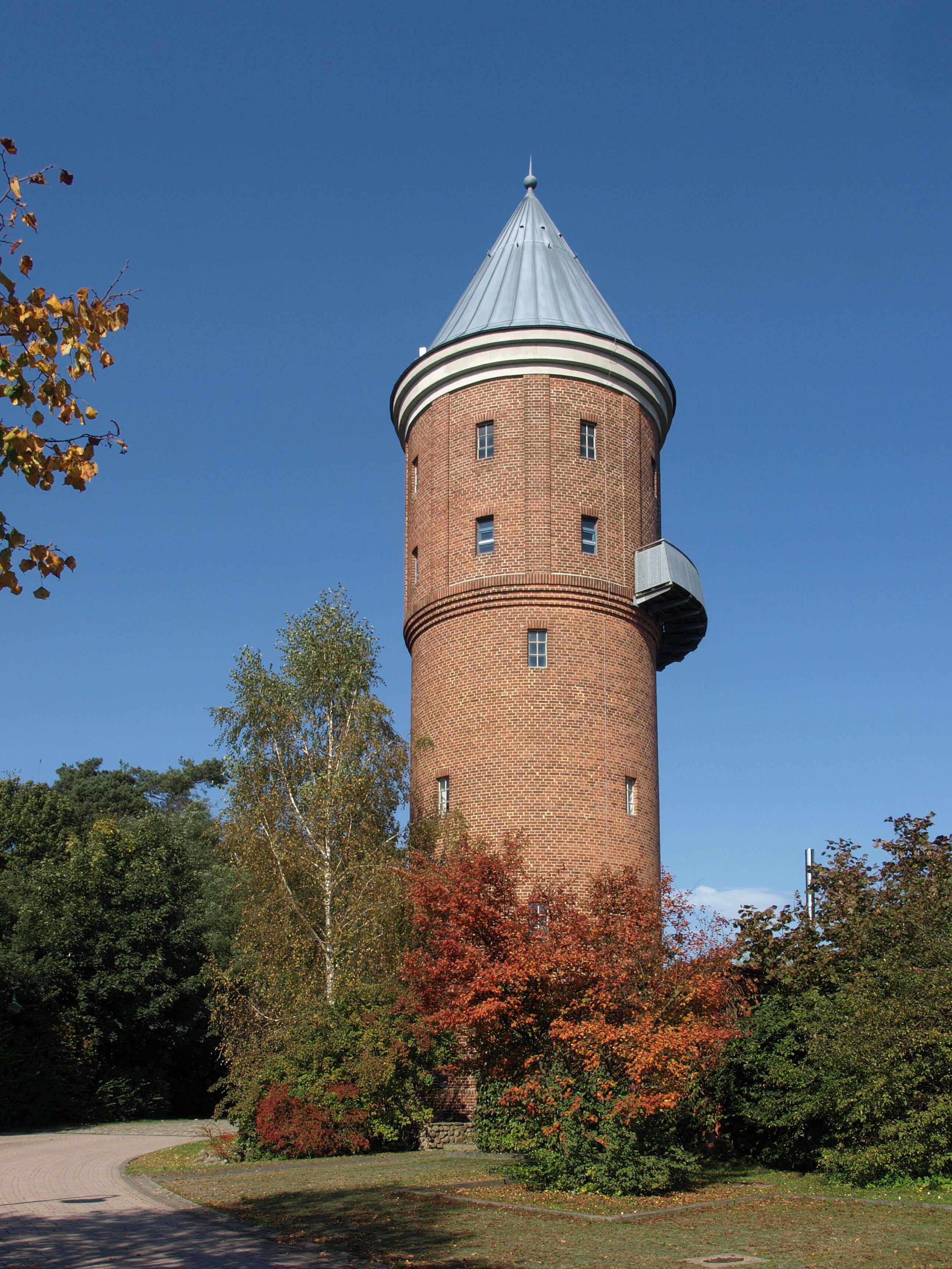 A tall brick tower with a conical roof, surrounded by autumn foliage and trees.