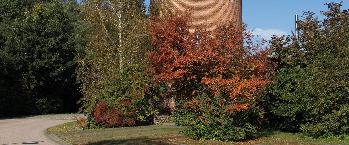 A tall brick tower with a conical roof, surrounded by autumn foliage and trees.