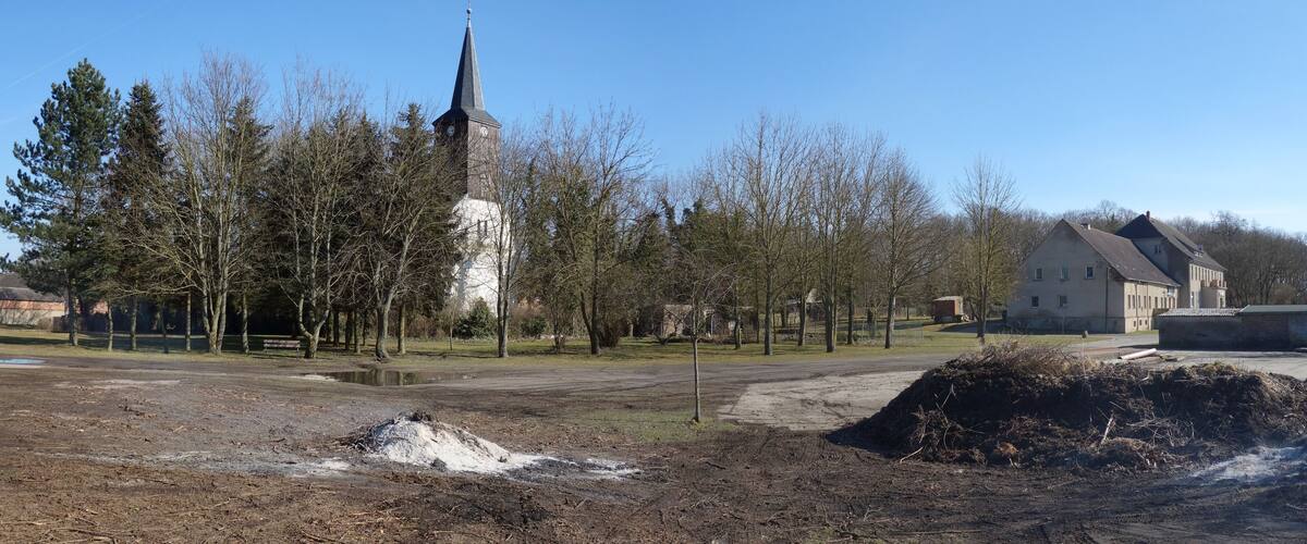 A church with a tall steeple, a large open field, and a building with a sloped roof.