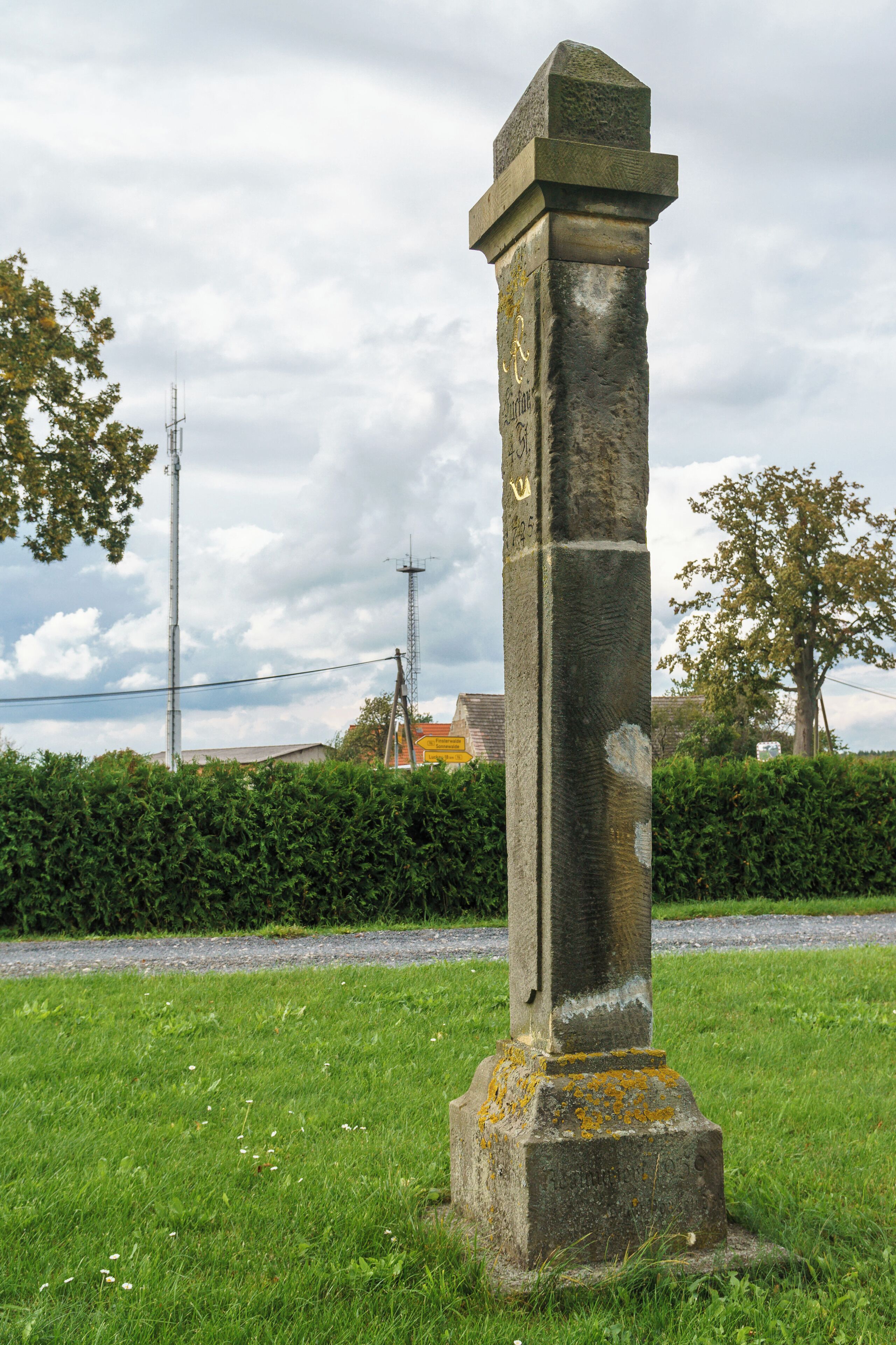 A tall stone monument with inscriptions, surrounded by grass and trees.