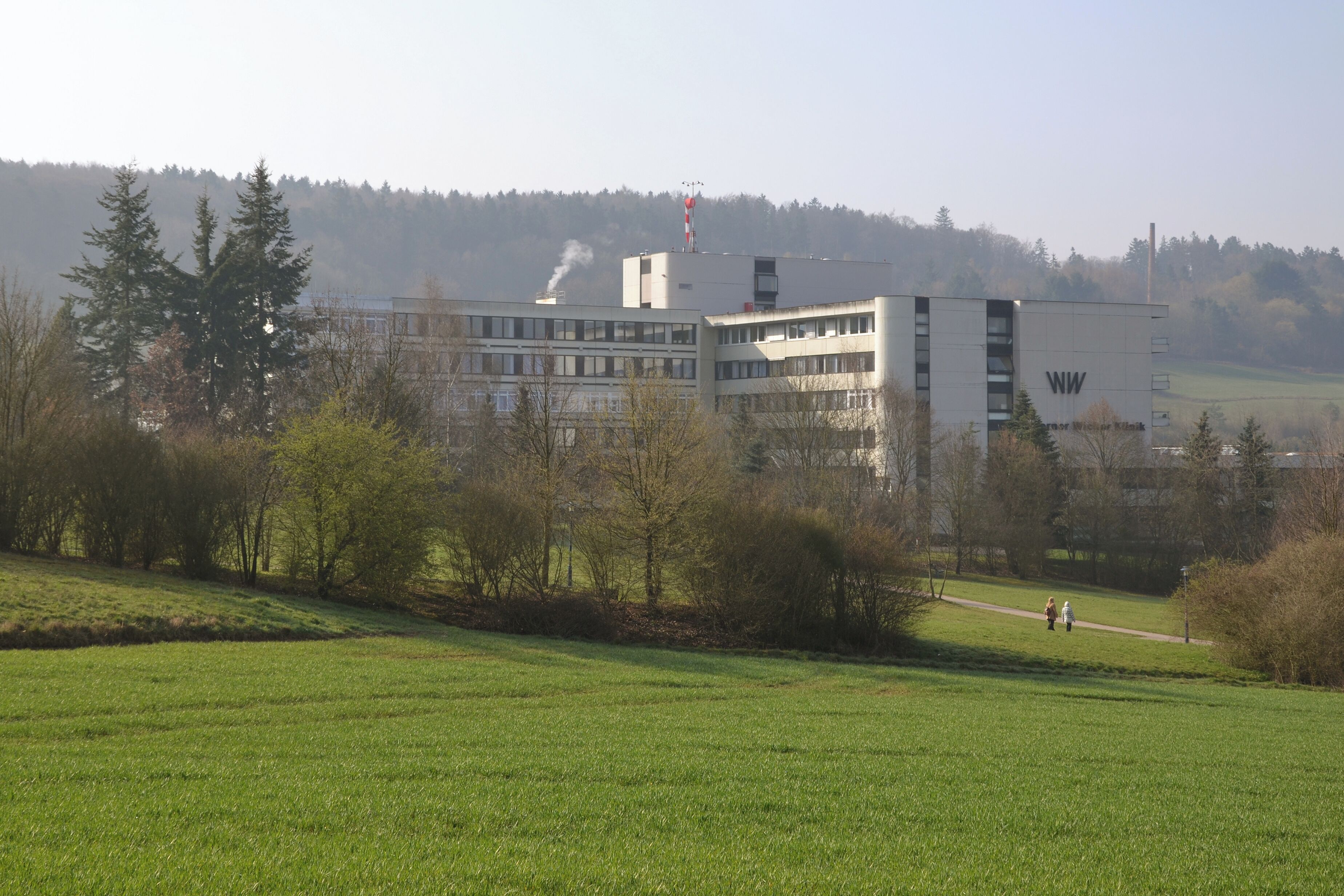 A building with 'WW' on its side, surrounded by a green field and trees.