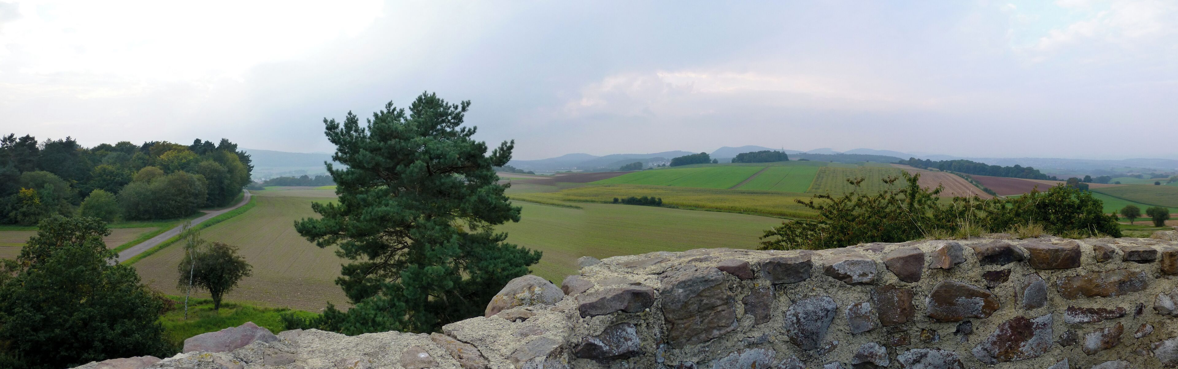 A stone wall with a view of rolling green fields and distant hills.
