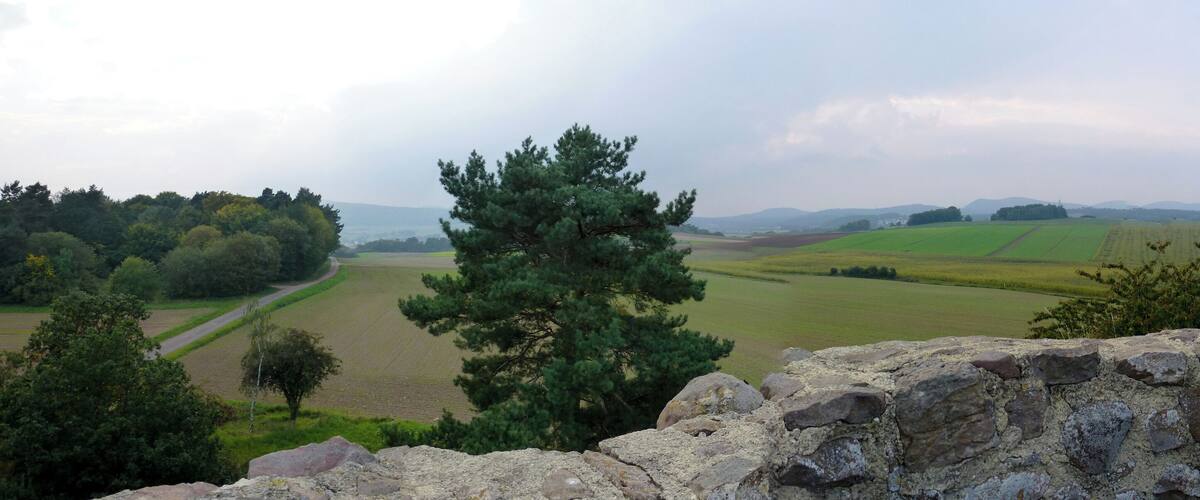 A stone wall with a view of rolling green fields and distant hills.