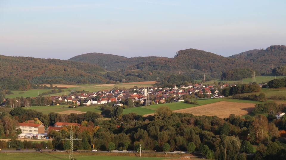 A rural landscape with rolling hills, a small village, and wind turbines.