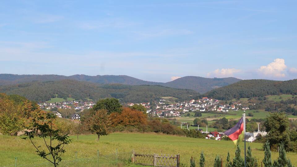A rural landscape with rolling hills, a small village, and a flag on a pole.