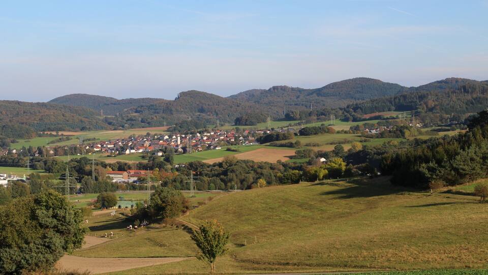 A rural landscape with rolling hills, a small village, and scattered houses.