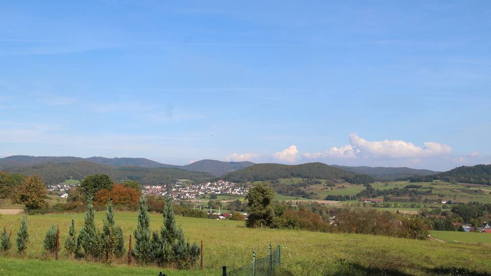 A rural landscape with rolling hills, a small town in the valley, and a clear blue sky.