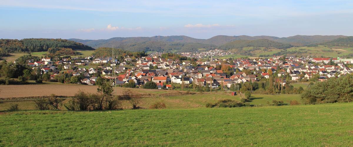 A village nestled in a valley with rolling hills in the background.