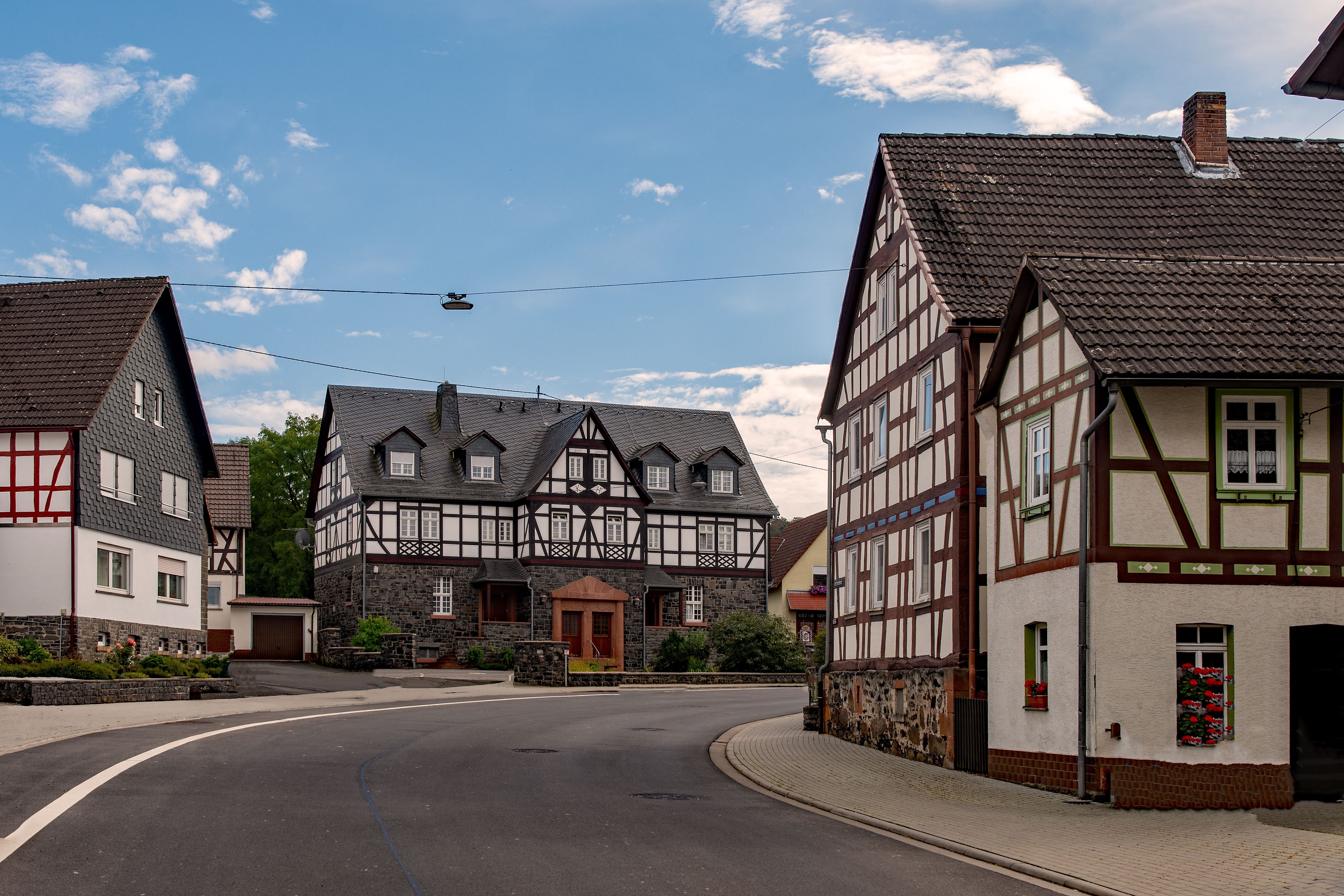 A street with traditional half-timbered houses, a clear sky, and a helicopter in the distance.
