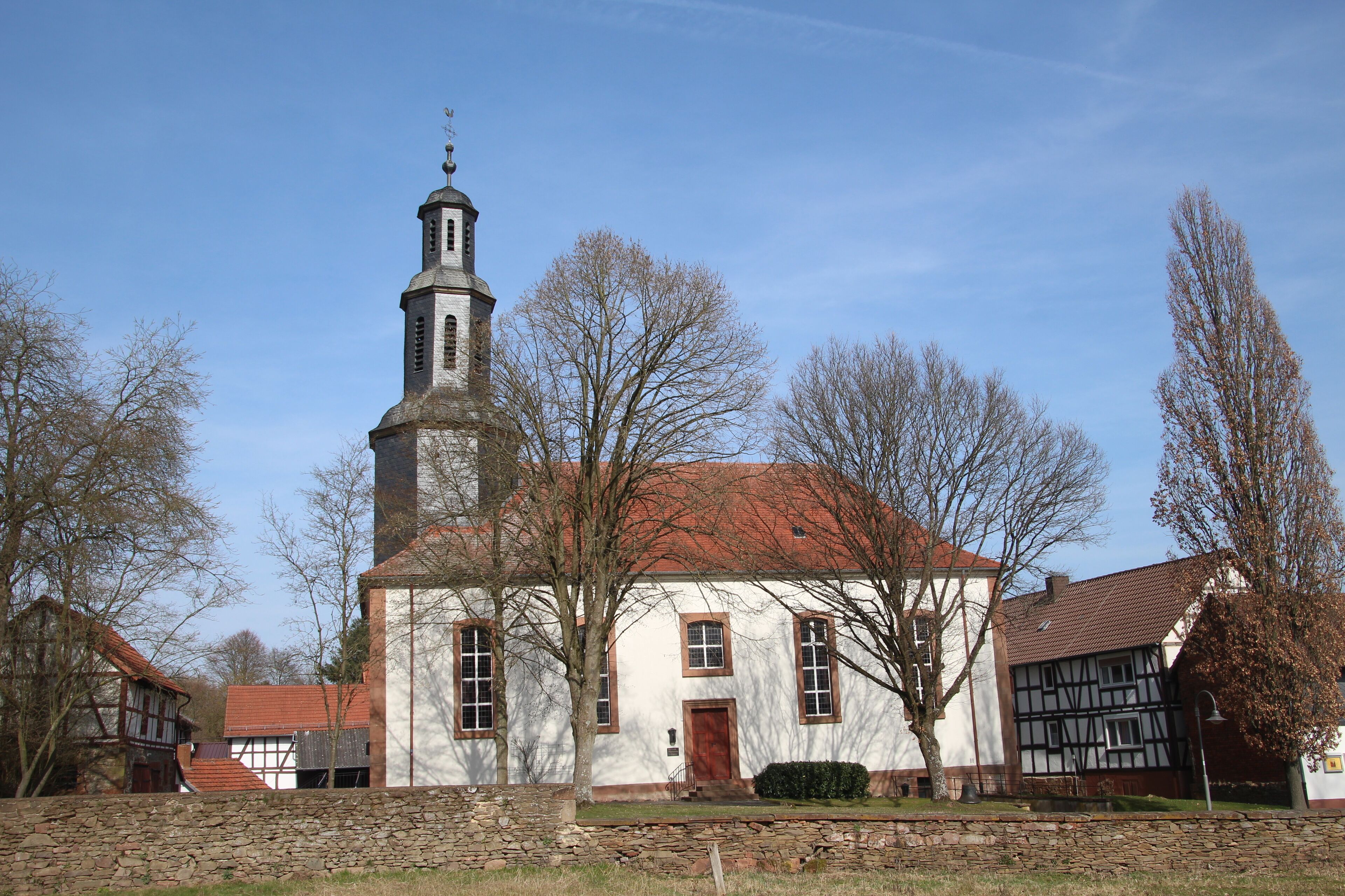 A church with a tall steeple and a red roof, surrounded by trees and other buildings.