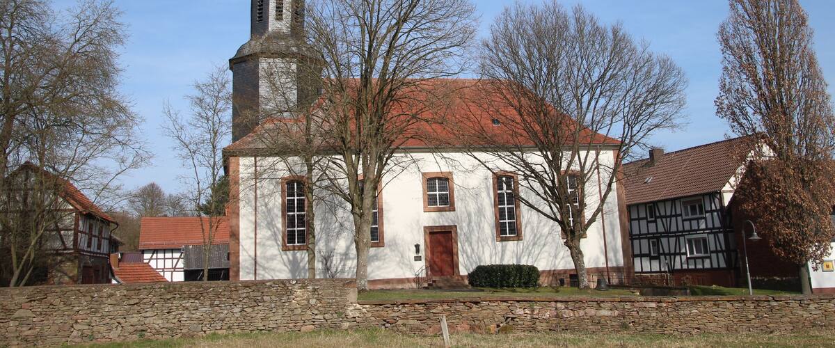 A church with a tall steeple and a red roof, surrounded by trees and other buildings.