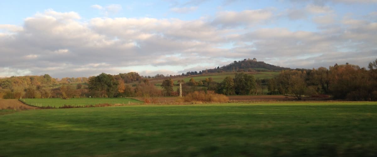 A green field with a hill in the background and a cloudy sky.
