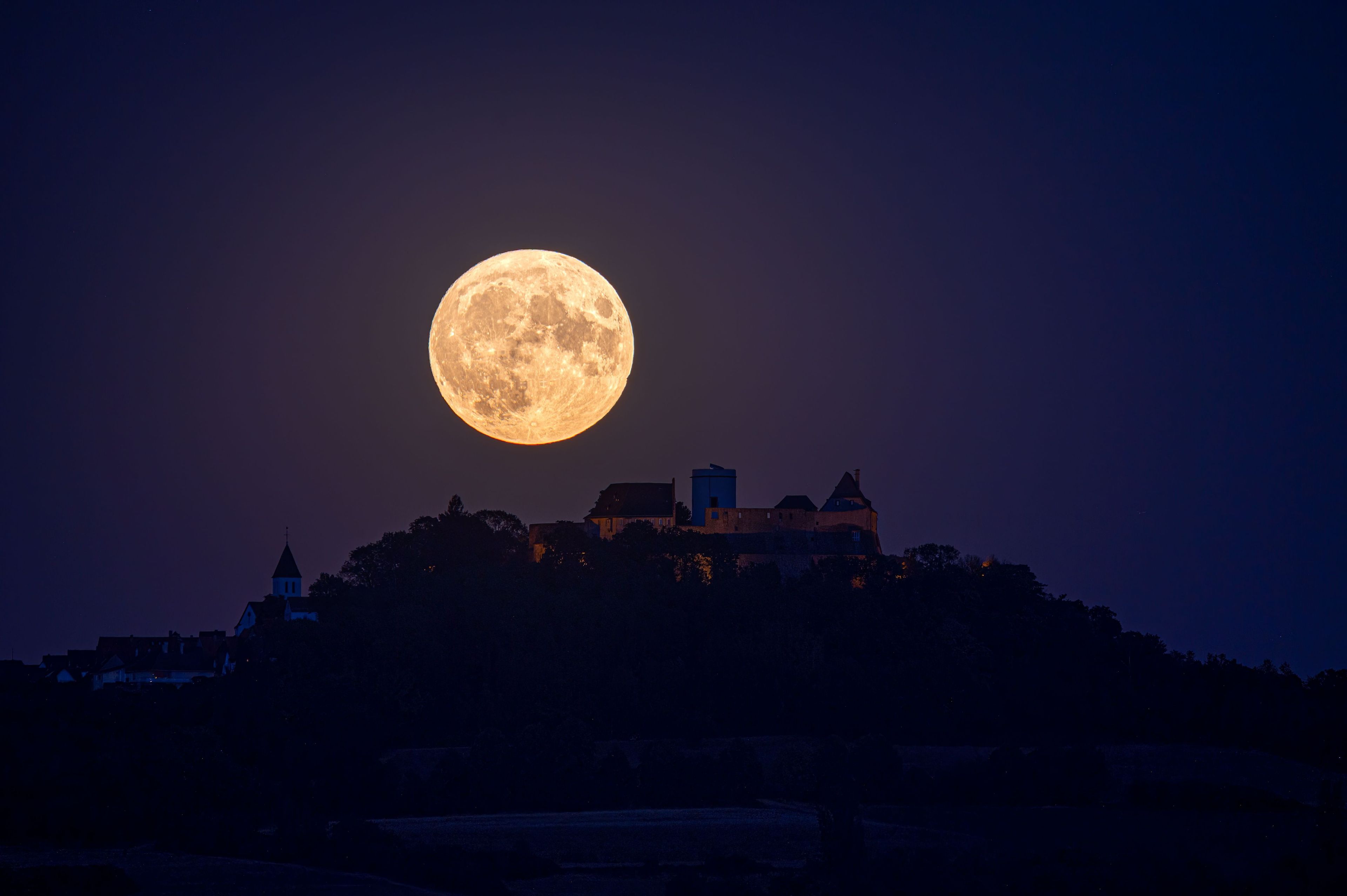A full moon illuminating a historic castle on a hill.