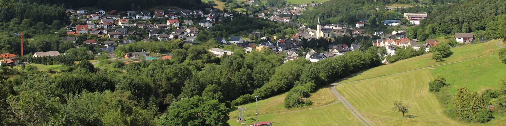 A town nestled in a valley with rolling hills, surrounded by lush greenery and a clear blue sky.