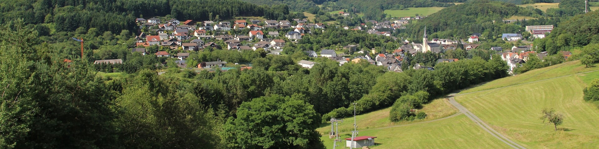 A town nestled in a valley with rolling hills, surrounded by lush greenery and a clear blue sky.