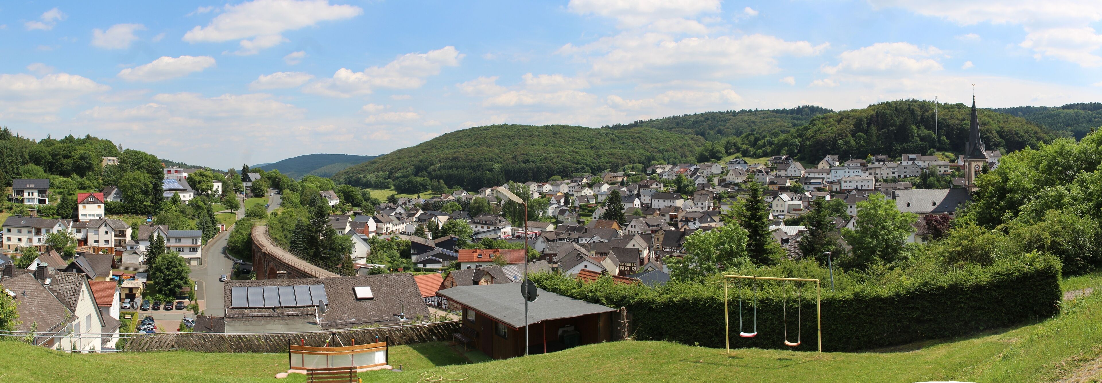 A town nestled in a valley with a river running through it, surrounded by hills and greenery.